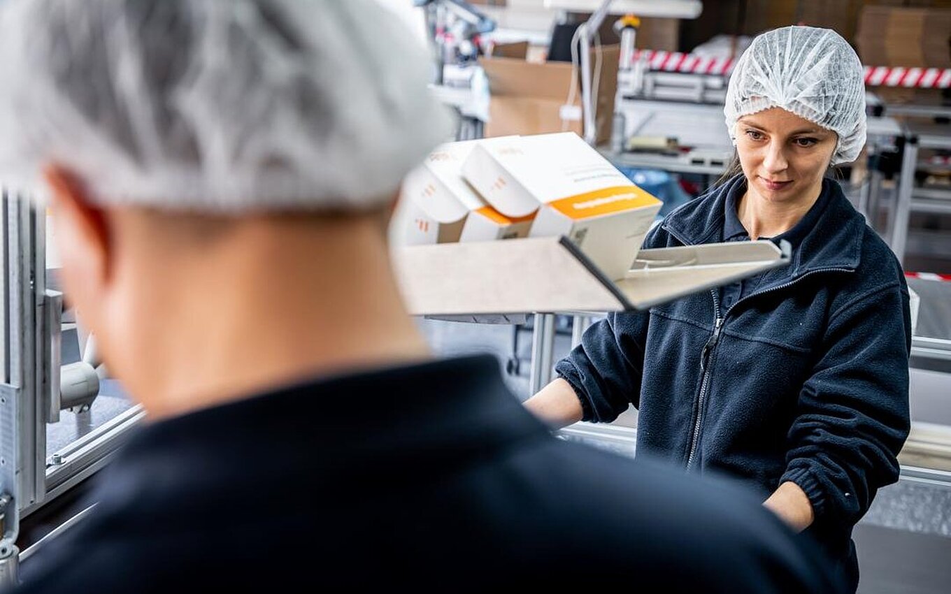 igne d’emballage efficace chez Faller Packaging – une employée contrôle des étuis pliants préconditionnés dans le service PrePackaging.