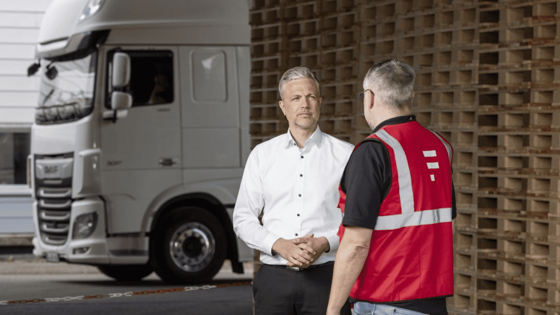 Wenn eine Bestellung Ihren Verpackungslieferanten an seine Grenzen bringt Zwei Personen im Gespräch vor einer Palettenwand, dahinter ist ein LKW.