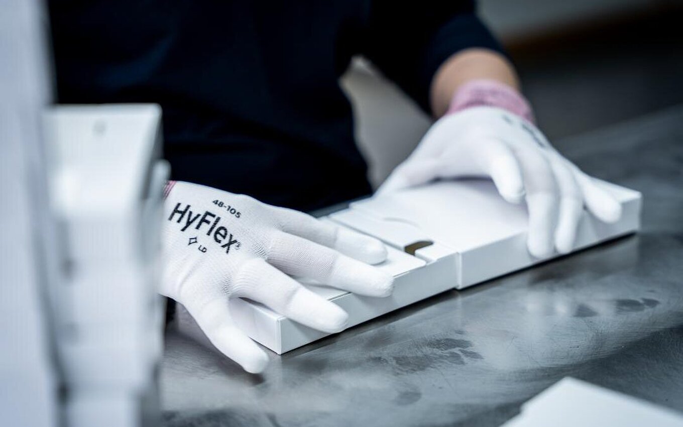 Travail manuel dans le service PrePackaging de Faller Packaging – un employé plie des emballages pharmaceutiques avec la plus grande précision.